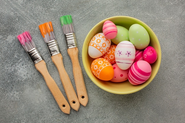 Foto gratuita vista superior de coloridos huevos de pascua en un tazón con pinceles