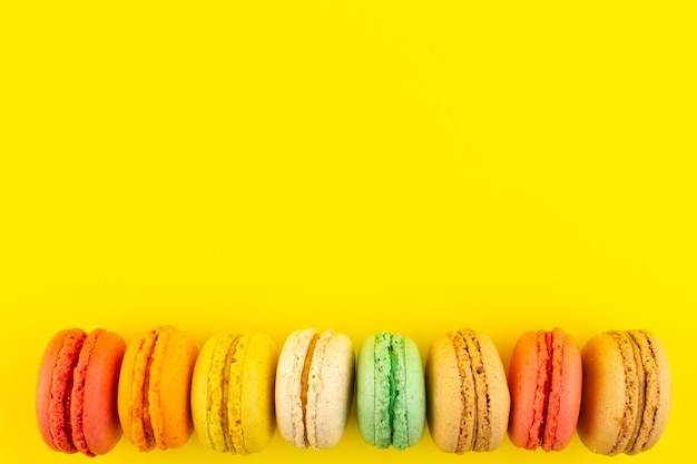 Una vista superior de coloridos macarons franceses deliciosos en el escritorio amarillo pastel de azúcar galleta dulce