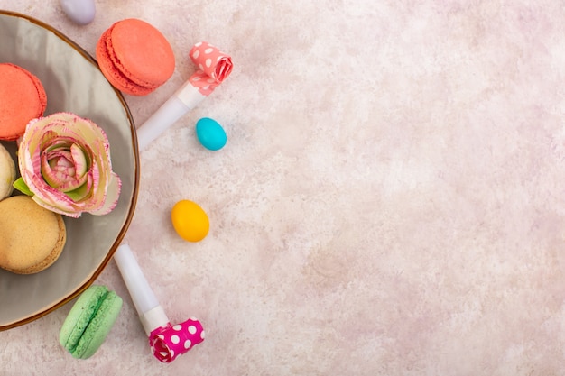 Una vista superior de coloridos macarons franceses deliciosos en el escritorio rosa pastel de azúcar galleta dulce