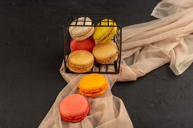 Una vista superior de coloridos macarons franceses deliciosos y horneados dentro de la canasta en la mesa oscura pastel galleta galleta azúcar