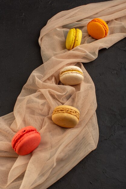 Una vista superior de coloridos macarons franceses deliciosos y horneados en la mesa oscura pastel galleta galleta azúcar