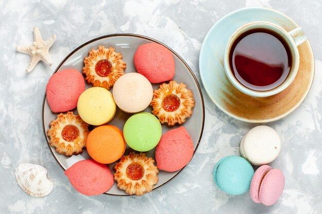 Vista superior coloridos macarons franceses deliciosos pasteles con galletas y té en la superficie blanca hornear pastel dulce azúcar postre galleta