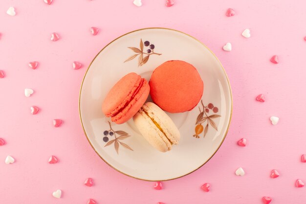 Una vista superior de coloridos macarons franceses dentro de la placa en el escritorio rosa pastel galleta azúcar dulce