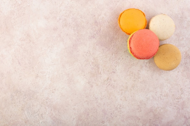 Una vista superior de coloridos macarons franceses formados y deliciosos en el escritorio rosa pastel de galletas de azúcar