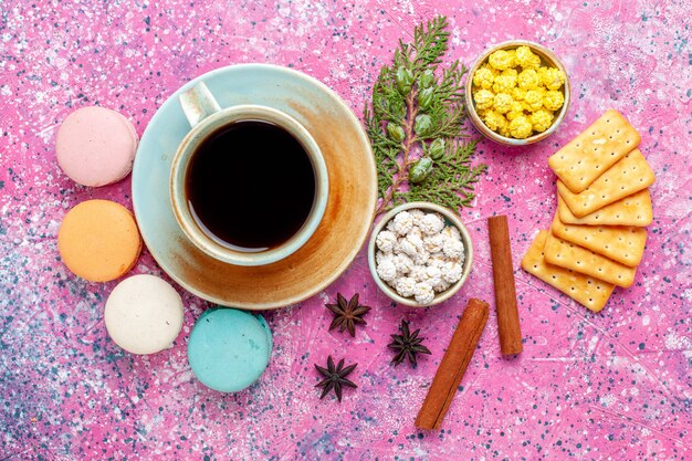 Vista superior de coloridos macarons franceses con galletas de canela y una taza de té en el escritorio rosa pastel hornear pastel de azúcar dulce color