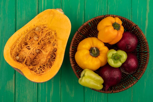 Vista superior de coloridos pimientos en un balde con cebolla roja con calabaza aislado en una pared de madera verde