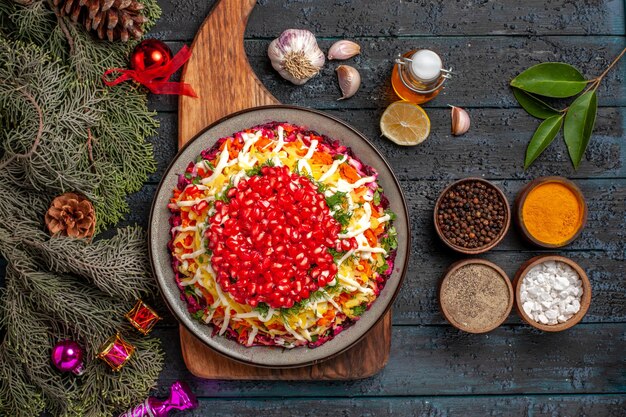 Vista superior de la comida navideña en el plato del tablero del plato navideño a bordo junto a las ramas con conos tazones de aceite de especias ajo limón