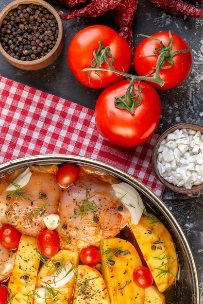 Foto gratuita vista superior de la comida de pollo crudo con patatas, verduras en una cacerola sobre una toalla roja pelada y sal de tomate sobre fondo gris