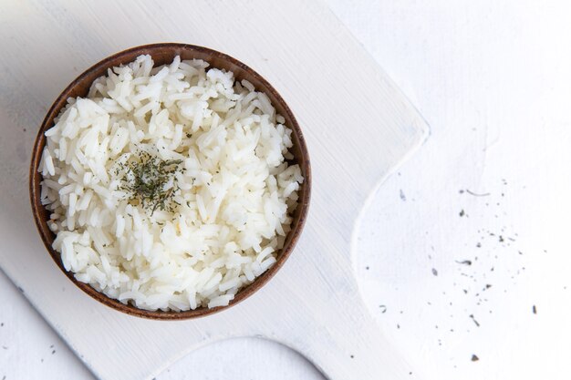 Vista superior de la comida sabrosa de arroz cocido dentro de una olla marrón con pimienta en la superficie blanca