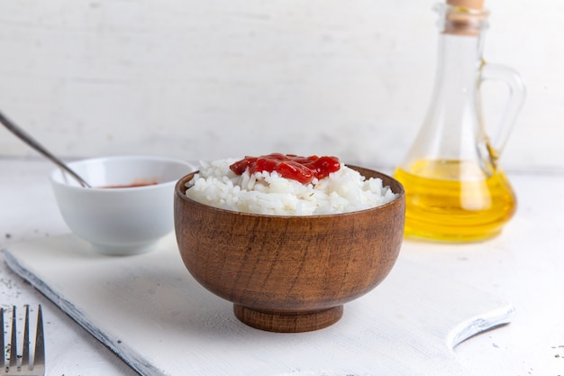 Vista superior de la comida sabrosa de arroz cocido dentro de una olla marrón con salsa picante y aceite en la superficie blanca