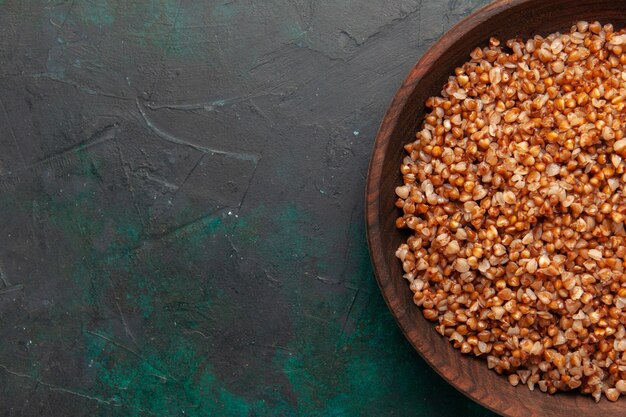 Vista superior de la comida sabrosa de trigo sarraceno cocido dentro de la placa marrón en el escritorio verde oscuro