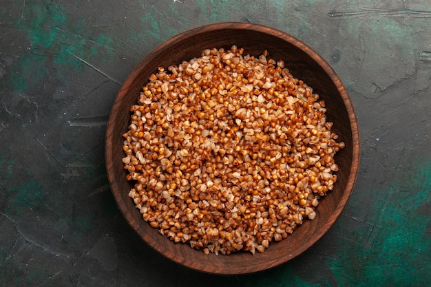 Vista superior comida sabrosa de trigo sarraceno cocido dentro de la placa marrón sobre la superficie verde oscuro