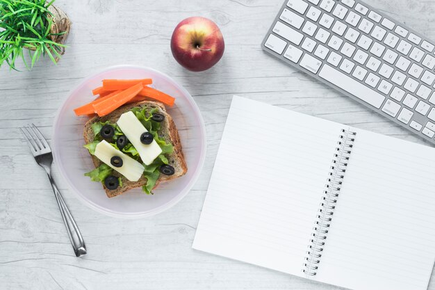 Vista superior de la comida saludable con libro espiral abierto y teclado de computadora inalámbrico en la mesa