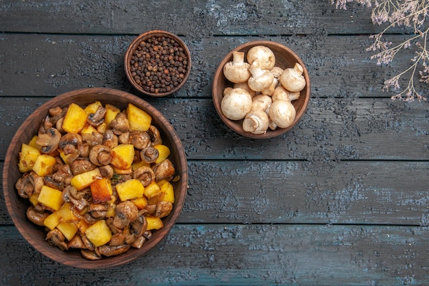 Vista superior de la comida en un tazón de fuente con patatas y champiñones junto a tazones de pimienta negra y champiñones blancos