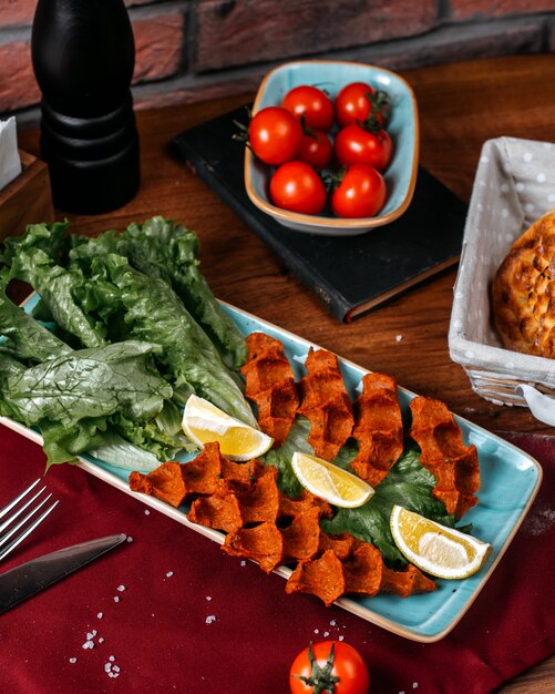 Vista superior de la comida turca cig kofte con limón y lechuga en una mesa de madera