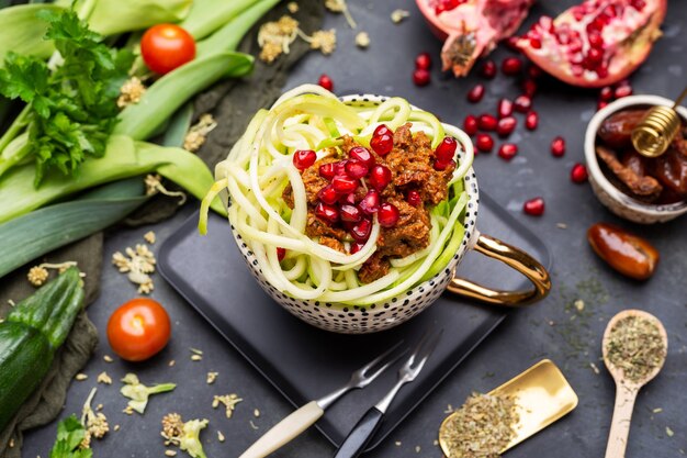 Vista superior de una comida vegana con calabacín en espiral, salsa de tomate y granadas en la taza