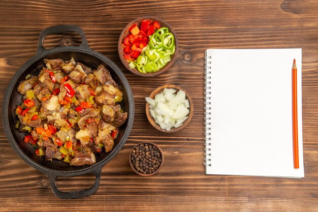 Vista superior comida vegetal cocida con carne y pimiento fresco en rodajas en el escritorio de madera marrón