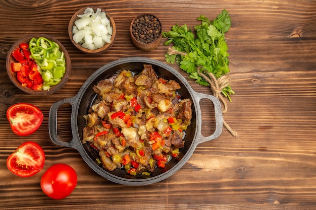 Vista superior comida vegetal cocida con carne y pimiento fresco en rodajas en el escritorio de madera marrón