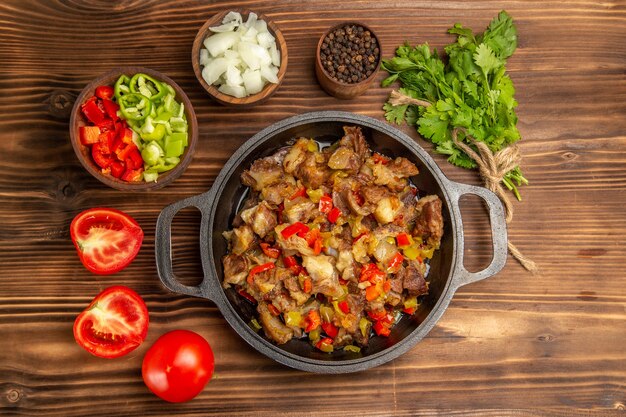 Vista superior comida vegetal cocida con carne y pimiento fresco en rodajas en el escritorio de madera marrón