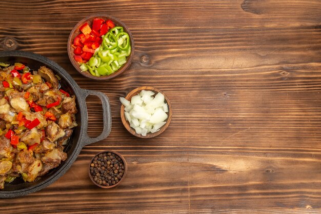 Vista superior comida vegetal cocida con carne y pimiento fresco en rodajas en el escritorio de madera marrón