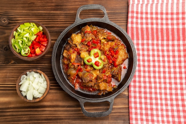 Vista superior de comida vegetal cocida con carne y pimiento en rodajas sobre la superficie de madera marrón