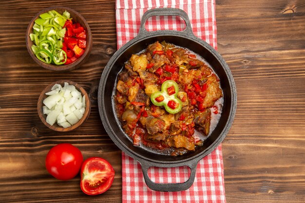 Vista superior de comida vegetal cocida con carne y pimiento en rodajas sobre la superficie de madera marrón