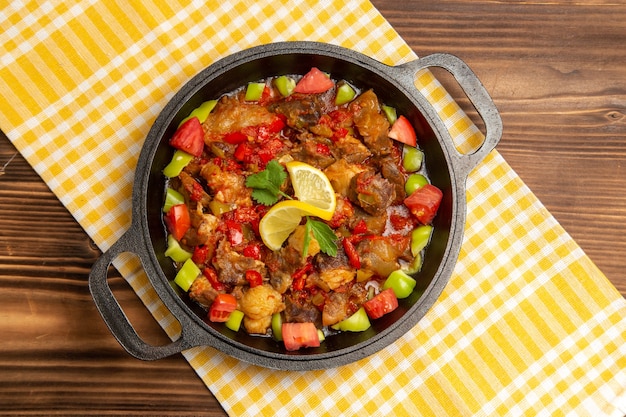 Vista superior de comida vegetal cocida con carne y pimientos en rodajas dentro de la sartén en el escritorio de madera marrón