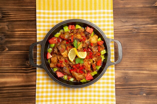 Vista superior de comida vegetal cocida con carne y pimientos en rodajas dentro de la sartén en el escritorio de madera