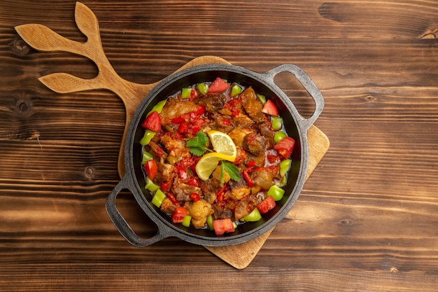 Vista superior de comida vegetal cocida con carne y pimientos en rodajas dentro de la sartén sobre superficie de madera marrón