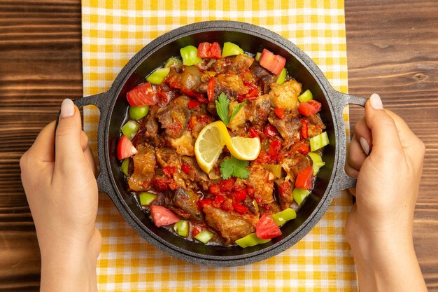 Vista superior de comida vegetal cocida con carne y pimientos en rodajas en el escritorio de madera marrón