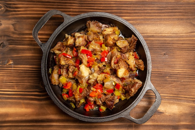 Vista superior de comida vegetal cocida con carne y pimientos en rodajas en el escritorio de madera