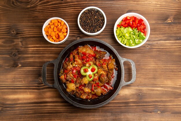 Vista superior de comida vegetal cocida con condimentos y pimiento en rodajas en el escritorio marrón