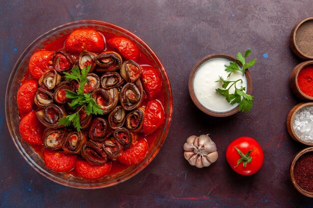 Vista superior comida vegetal cocida deliciosos tomates y berenjenas con condimentos en el escritorio oscuro
