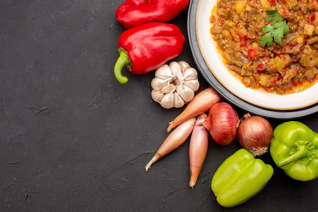 Vista superior de comida vegetal cocida dentro de la placa con verduras frescas en el plato de comida de fondo gris