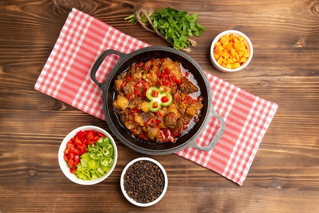 Vista superior de comida vegetal cocida que incluye salsa de verduras y carne dentro de un escritorio marrón