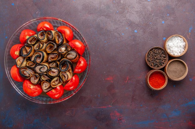 Vista superior de la comida vegetal en rodajas y tomates enrollados con berenjenas y condimentos en el escritorio de color púrpura oscuro