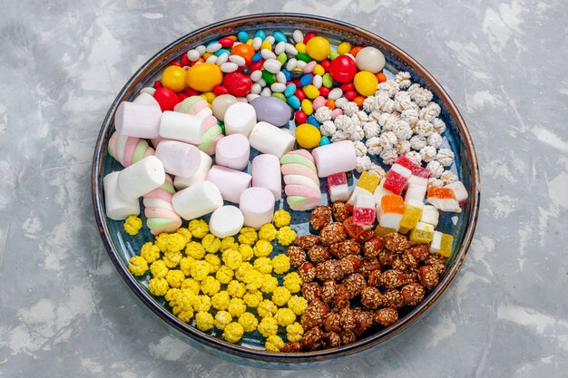 Vista superior de la composición de dulces caramelos de diferentes colores con malvavisco en el escritorio blanco claro caramelo de azúcar bombón confitura dulce