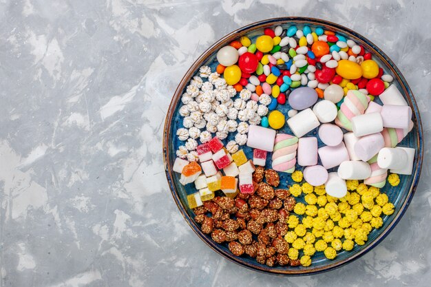 Vista superior de la composición de dulces caramelos de diferentes colores con malvavisco en el escritorio blanco dulces de azúcar bombón confituras dulces