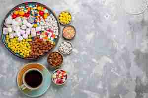 Foto gratuita vista superior de la composición de dulces caramelos de diferentes colores con malvavisco y una taza de té en el escritorio blanco azúcar caramelo bombón confitura dulce