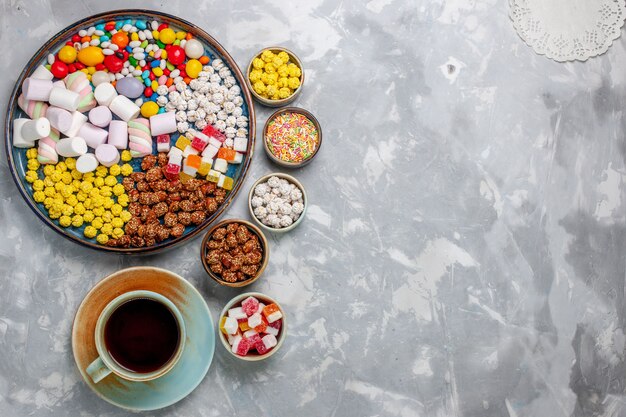 Vista superior de la composición de dulces caramelos de diferentes colores con malvavisco y una taza de té en el escritorio blanco azúcar caramelo bombón confitura dulce