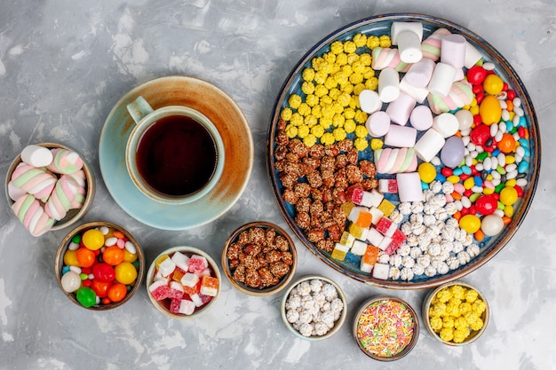 Foto gratuita vista superior de la composición de dulces caramelos de diferentes colores con malvavisco y una taza de té en el escritorio blanco azúcar caramelo bombón confitura dulce