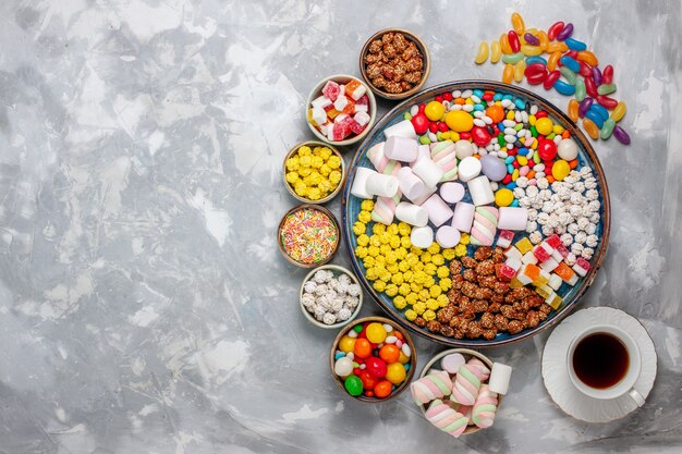 Vista superior de la composición de dulces caramelos de diferentes colores con malvavisco y té en el escritorio blanco bombones de azúcar confites dulces dulces