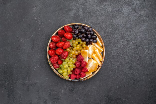 Vista superior de la composición de frutas fresas uvas frambuesas y mandarinas dentro de la bandeja en el espacio oscuro