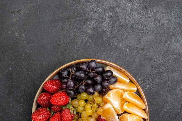 Vista superior de la composición de frutas fresas uvas frambuesas y mandarinas dentro de la bandeja en el espacio oscuro