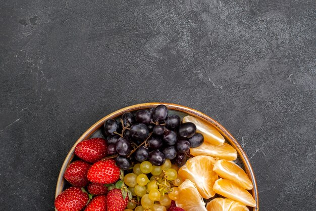 Vista superior de la composición de frutas fresas uvas frambuesas y mandarinas dentro de la bandeja en el espacio oscuro