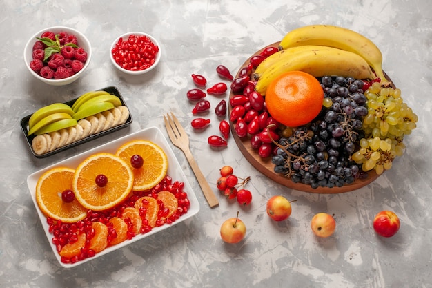 Foto gratuita vista superior de la composición de frutas frescas, cornejos, uvas, plátanos y naranjas sobre superficie blanca clara, jugo de vitamina de frutas, vitamina suave