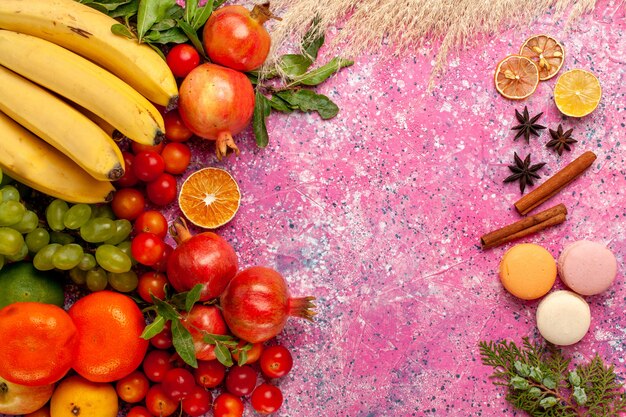 Vista superior de la composición de frutas frescas con macarons franceses en una superficie de color rosa claro