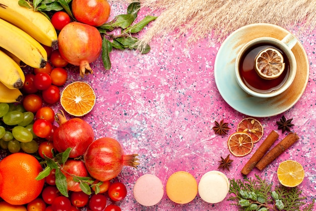 Vista superior de la composición de frutas frescas con macarons franceses y té en una superficie de color rosa claro