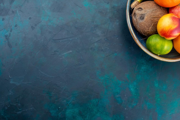 Vista superior de la composición de frutas mandarinas plátanos manzanas y coco en el escritorio azul oscuro