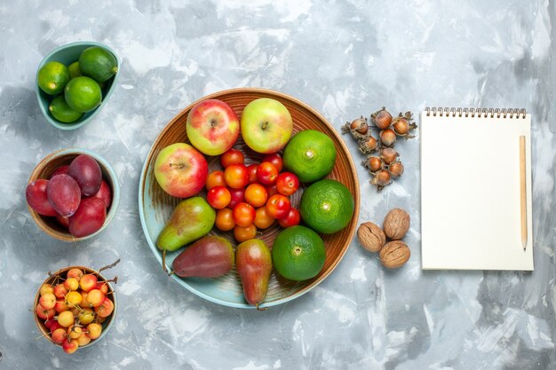 Vista superior composición de frutas manzanas peras nueces mandarinas y ciruelas en el escritorio blanco.